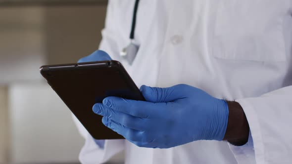 African american senior male doctor wearing white coat using digital tablet