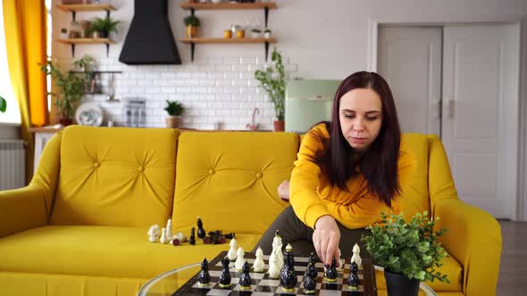 Young Woman Sitting on Yellow Sofa and Playing Chess in Room