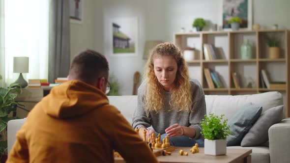 Smiling Young Adult European Couple Play Chess at Home