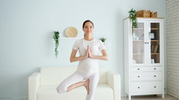 Pregnant Woman Stands in Vrksasana in Spacious Room at Home