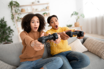 nd amazing modern video games. Shocked excited young african american ladies with open mouths have fun with joysticks, play in living room, free space