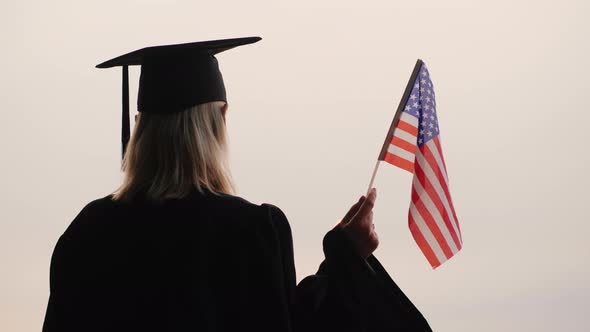 Student in Graduate Uniform with USA Flag in Hand