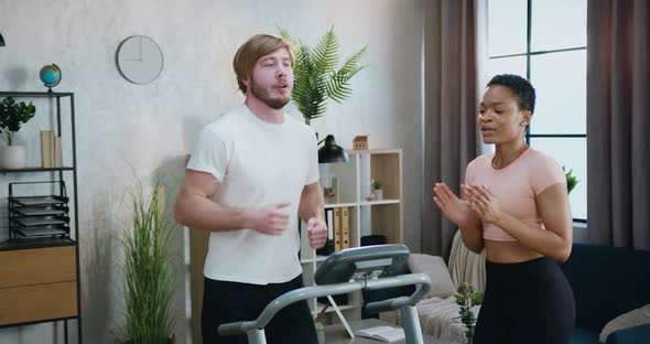 Guy in Sportswear Running on Treadmill while His Fit  African American Female Friend Supporting Him