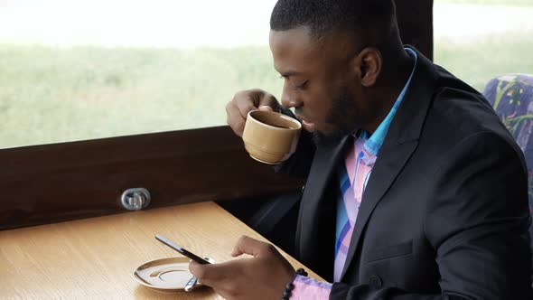 Afro American Businessman is Typing a Message on Smartphone Sitting in Cafe