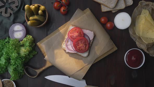 Flat Lay of the Sandwich with Sliced Ham and Vegetables on the Wooden Board in the Beam of Light