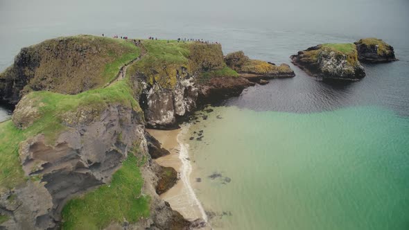 Ireland People Ocean Bay Aerial View: Tourists Walking on Carrick Islet, Carrick-a-Rede Rope Bridge