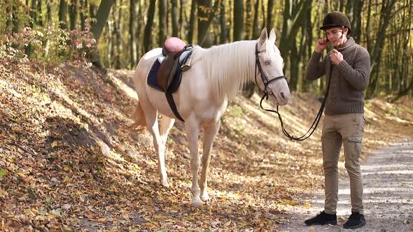 Young guy with white horse in autumn forest