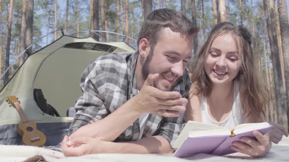 Portrait Bearded Man and Cute Young Woman Lying Near Each Other in the Tent in the Forest Reading