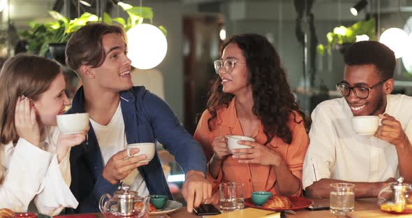 Good Looking Guy Holding Cup While Telling Funny Story To Friends in Cosy Cafe. Cheerful Young