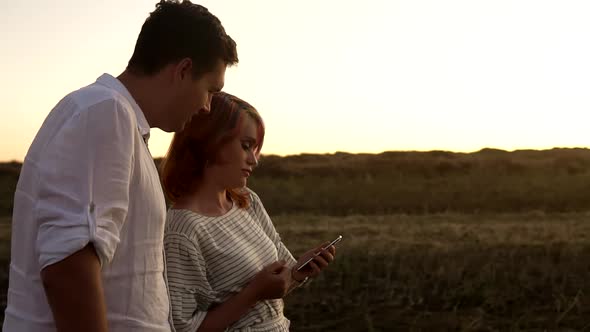 Slow Motion of Man and Woman Who are Standing in Summer Field on Sunset and Looking at Smartphone