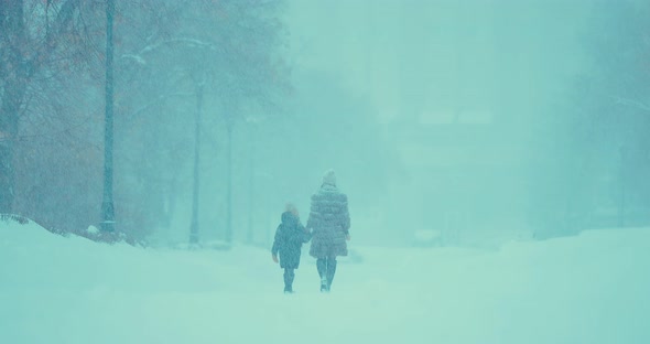 In Heavy Snowfall a Woman with a Child is Walking Along the Road