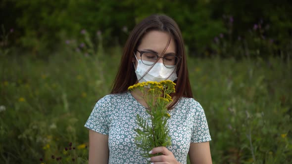 A Young Woman in a Medical Mask Sniffs Flowers and Does Not Smell