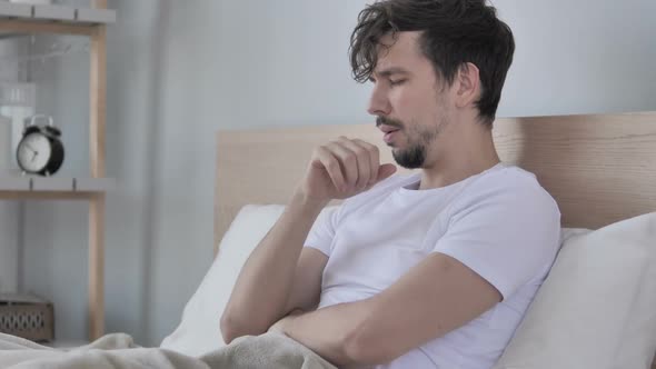 Sick Young Casual Man Coughing While Sitting in Bed