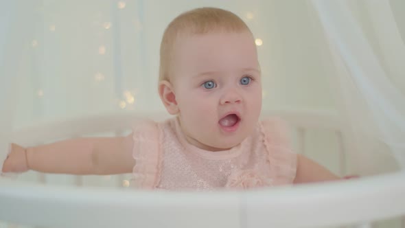 Close Up of Wondering 10 Months Old Baby Girl with Blue Eyes Sitting in Bed with Canopy with Lights