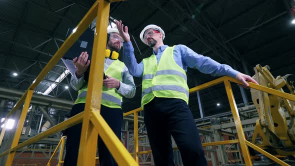 Workers Stand in a Factory Interior, Checking Equipment.