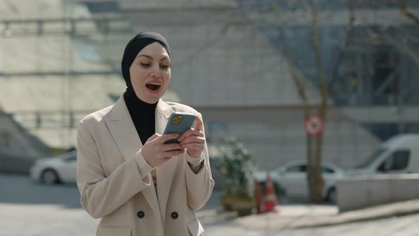 Arabian Businesswoman Dressed in Hijab Using Smartphone Walking in Business Quartal Having Good News