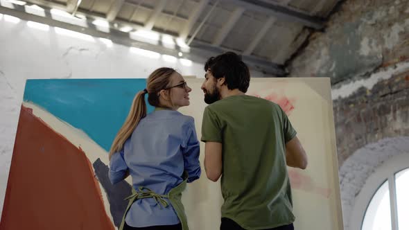 Young Couple Paints on Canvas Drawing Picture in Art Studio and Kissing