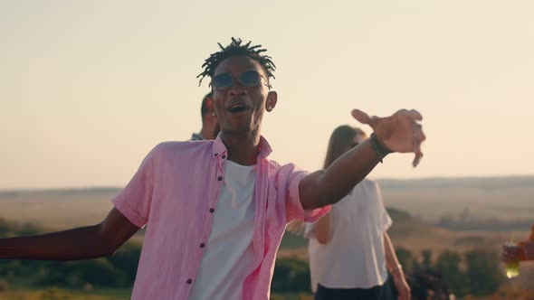 Black Man with Dreadlocks Dances and Sings Against the Background of His Friends