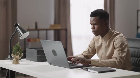 Concentrated Man is Working with Laptop in Home Office Afroamerican is Viewing Screen of Notebook