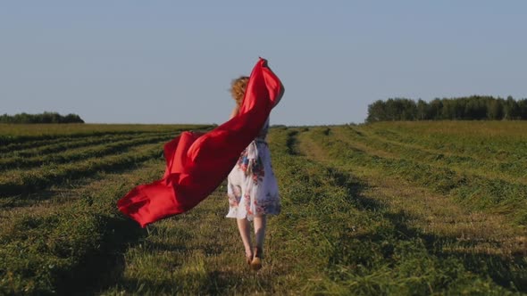 Redhead Woman in White Dress with Red Cloth in Her Hands on Background of Field