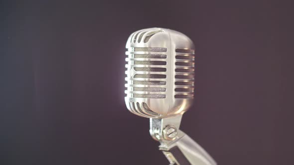 A vintage elvis microphone in front of a dark background with a light source out of frame. Shot in 4