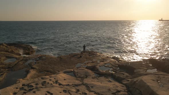 Breathtaking aerial view of a fisherman fishing on flat rocks with the light of the setting sun refl