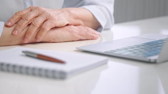 Senior woman puts overworked folded wrinkly hands on white table