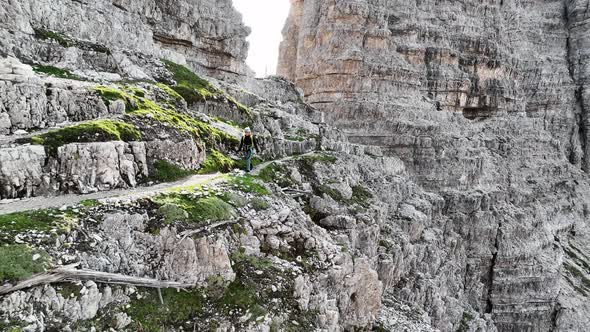 Female mountaineer with climbing gear in the Dolomites walking on a path. Wide shoot.