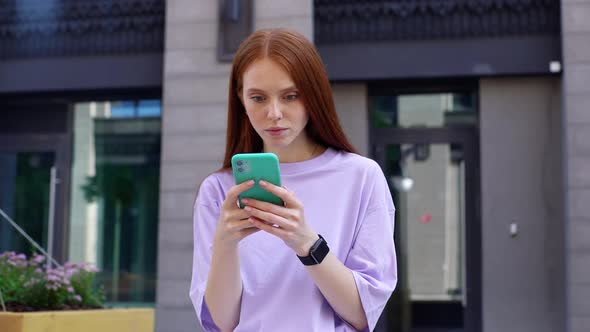 Portrait of Excited Redhead Young Woman Receiving Good News on Cellphone Outdoors.