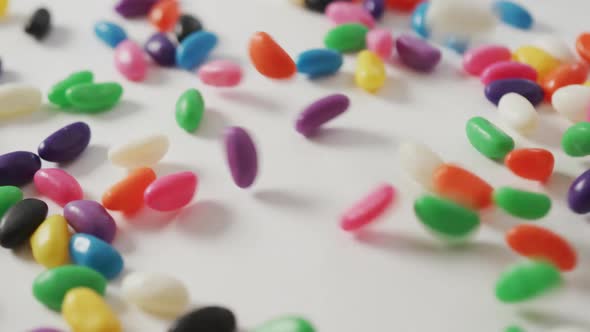 Video of close up of multi coloured sweets falling over white background