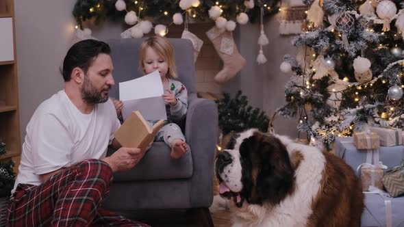 A Man Father Is Reading a Book To a Little Boy on Christmas Day Their Big Kind Dog Lies Nearby