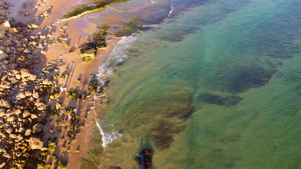 Amazing scenic drone aerial view of the beach and ocean with calm waves during a sunset