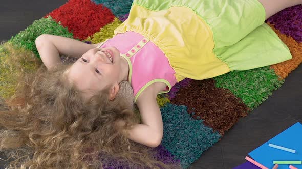 Beautiful Little Girl Lying on Colorful Carpet at Home