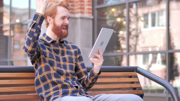 Man Cheering for Success on Tablet while Sitting on Bench