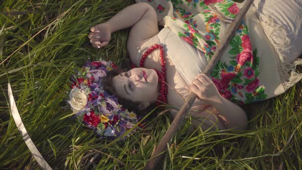 Portrait of Carefree Overweight Woman with a Wreath on Her Head Lying on the Grass in Summer Field