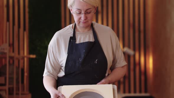 An Eldery Woman Showing a Clay Plate on the Wooden Desk