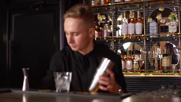 Medium Shot of Professional Young Bartender Scooping Ice Cubes and Putting in Shaker Standing in Bar