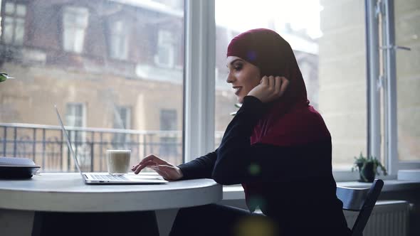Attractive Muslim Girl with Hijab Covering Her Head is Looking and Smiling at Something on Her