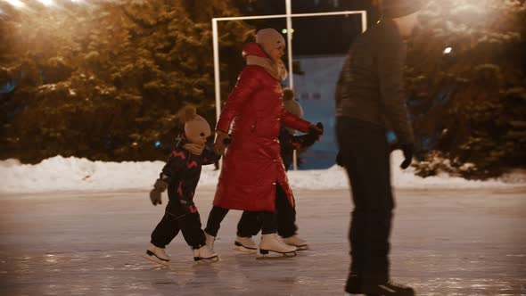 A Family of Young Mother and Two Kids Skating on the Ice Rink Holding Their Hands