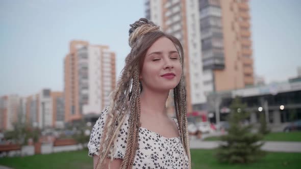 A Cute Young and Happy Girl with Dreadlocks Walks Down the Street and Poses