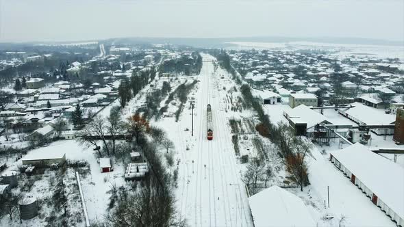 Aerial drone view of a moving train in a village, winter, Moldova. Railroad, station, residential bu