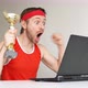 Sportsman celebrating victory with golden cup while watching result on laptop. - VideoHive Item for Sale