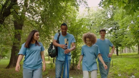 Young Male Leader Handing Out Litter Sticks to Volunteers Outdoors