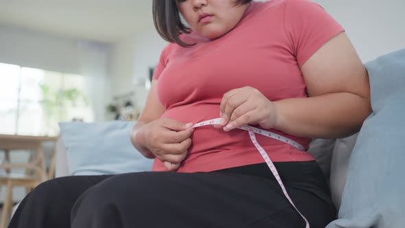 Asian young oversize women use tape measuring waist feeling ashamed and think to lose weight.