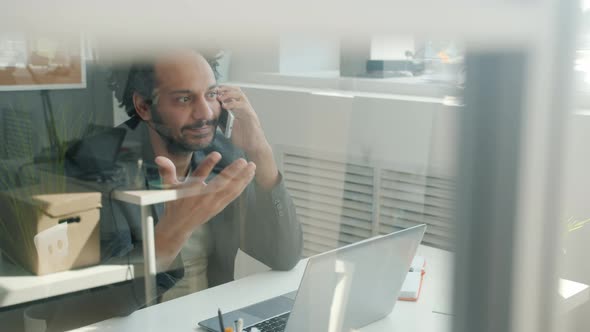 Middle Eastern Office Worker Talking on Mobile Phone and Smiling in Modern Glass Wall Office