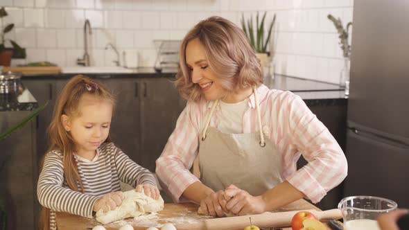 Young Woman with Her Little Daughter Kneads Dough on the Kitchen Table at Home They Prepare Pizza