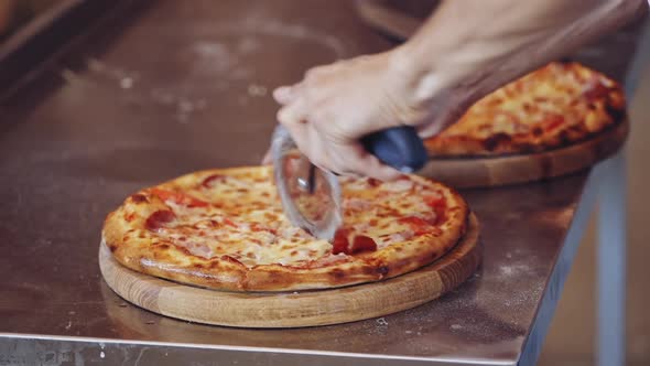 Italian pizza preparation. Close up hands of chef baker cutting pizza