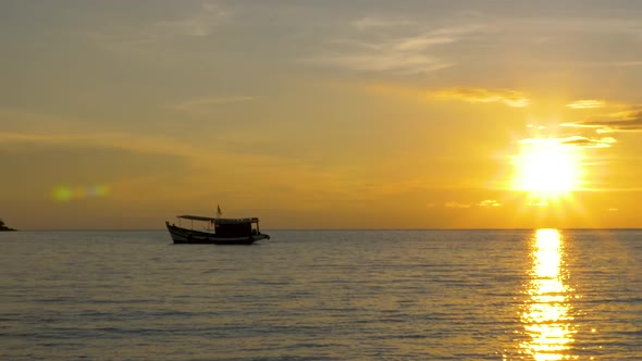 Silhouette of a fishing boat on the horizon with the sun setting in the background. ZOOM OUT