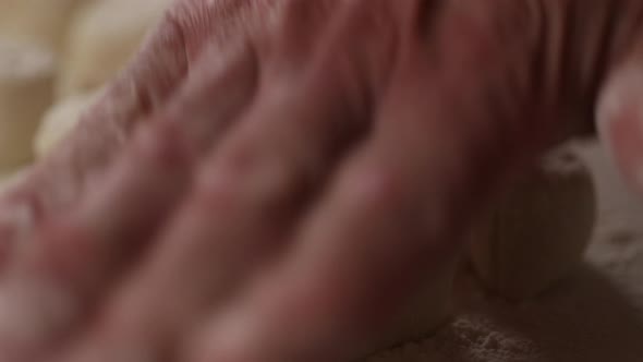 Chef sprinkles flour on balls of dough, then flattens them with his hand. Close up shot.