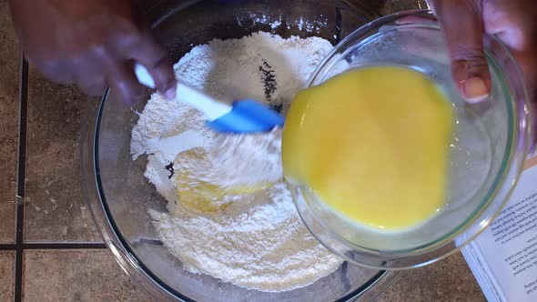 Pouring egg mixture into flour and stirring with spatula to make batter, Closeup